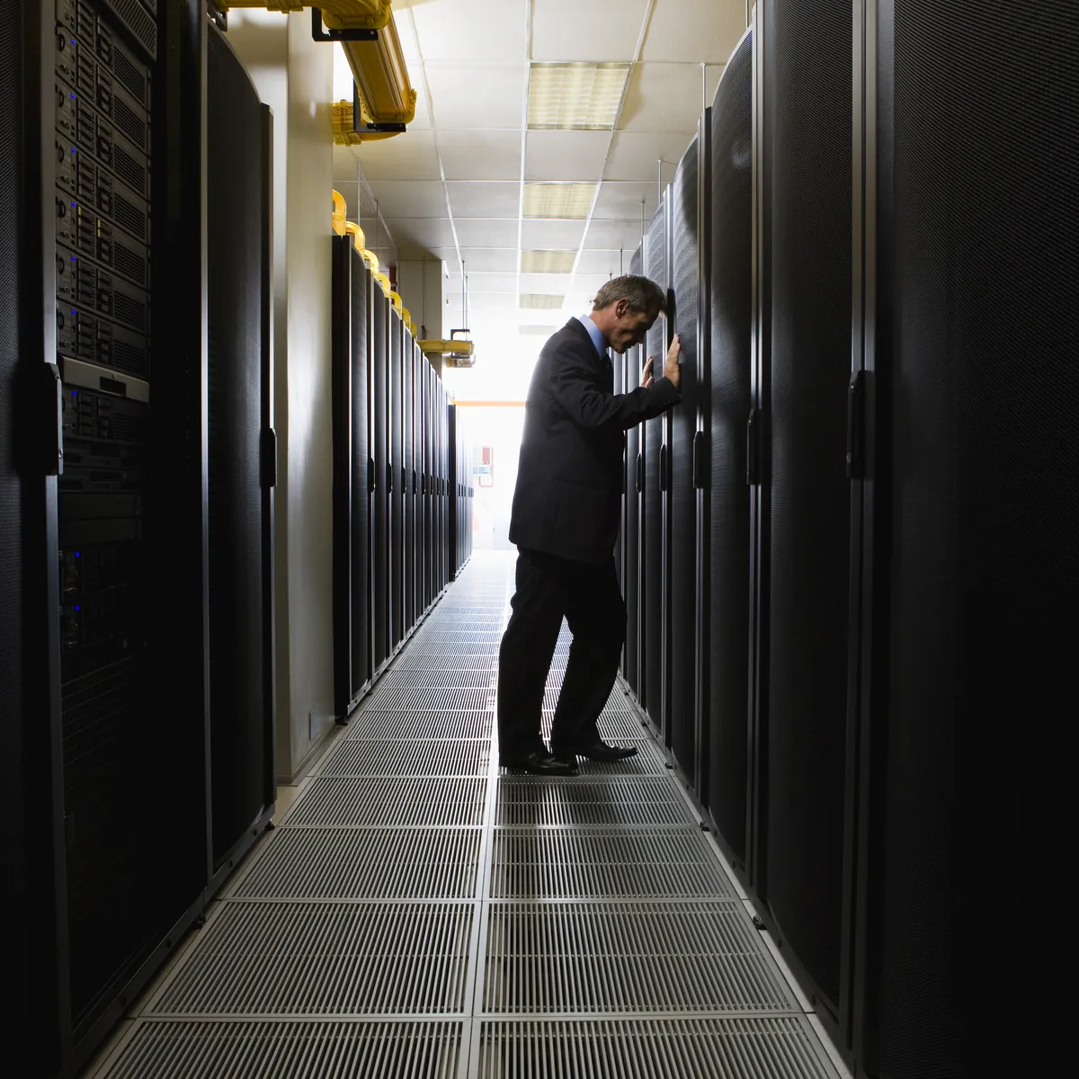 A man in a suit leaning against a rack in a long, brightly lit server corridor