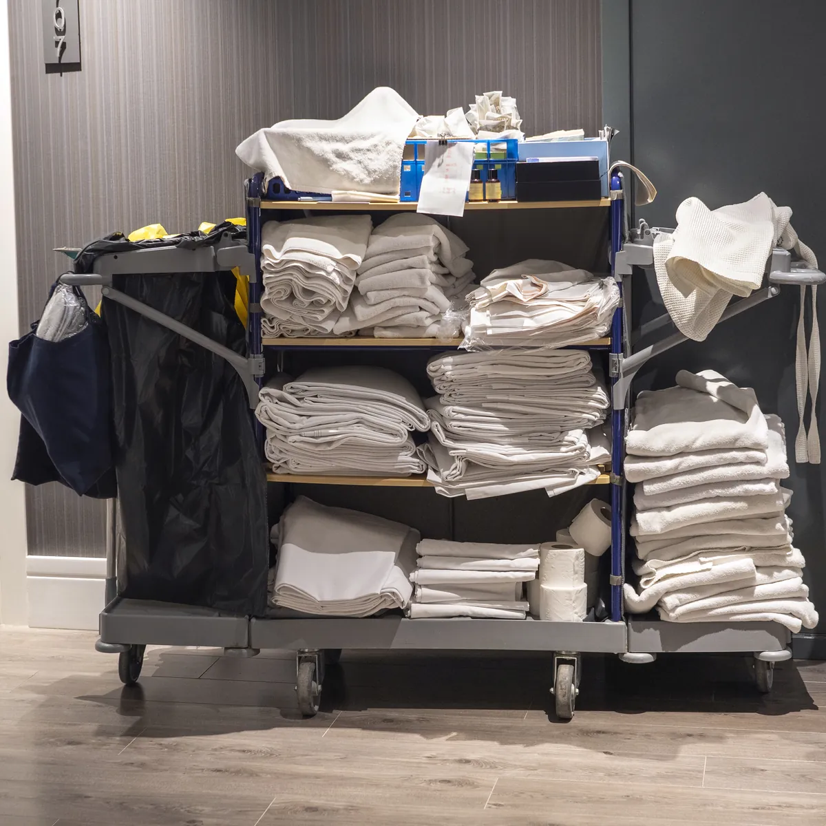 A housekeeping cart stacked with folded white linen in a hotel corridor
