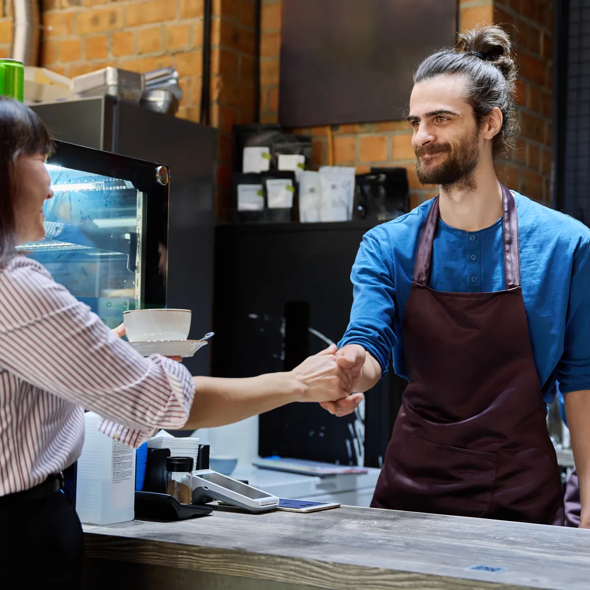 A barista shaking hands with a customer at a cafe counter