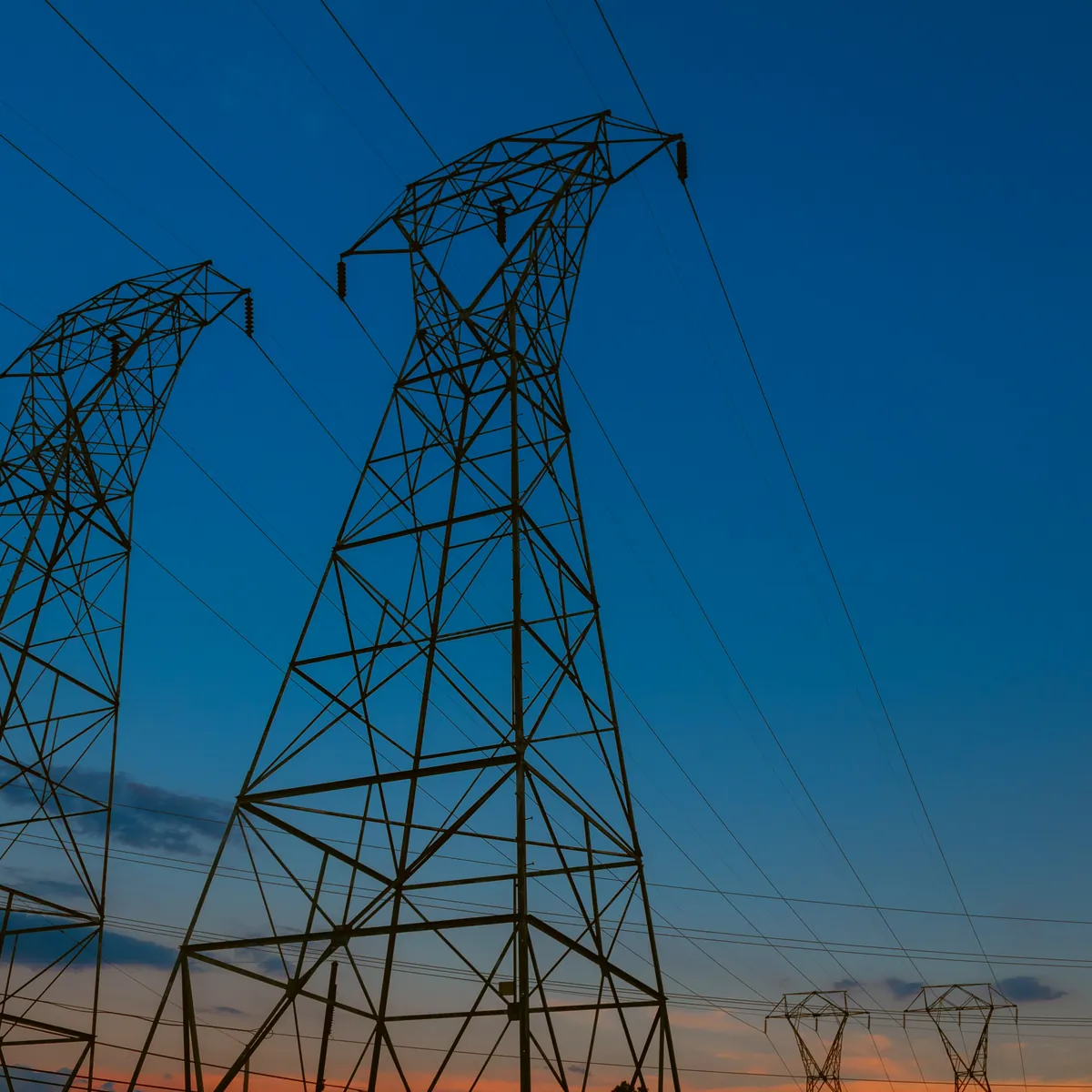 Steel transmission pylons and power lines silhouetted against a deep blue dusk sky