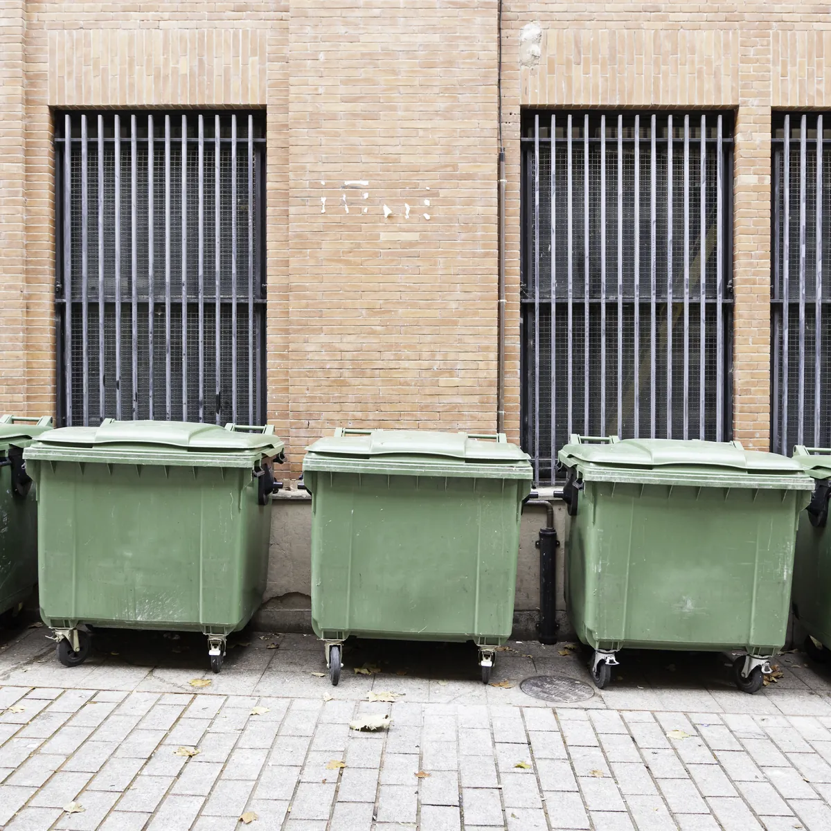 A row of green commercial waste containers against a brick building